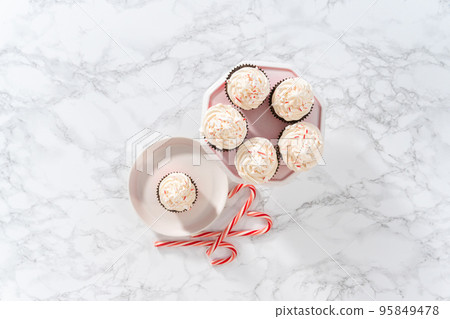 Flat lay. Freshly baked chocolate cupcakes with peppermint frosting and decorating with crushed peppermint candy cane candies. 95849478