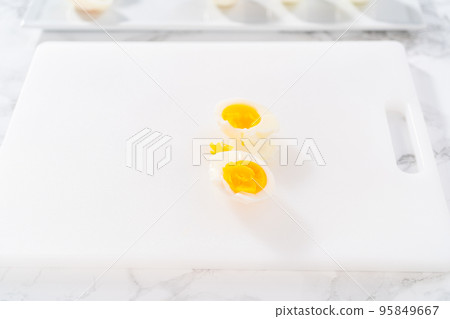 Slicing hard-boiled eggs on a white cutting board. Slicing hard-boiled eggs on a white cutting board. 95849667