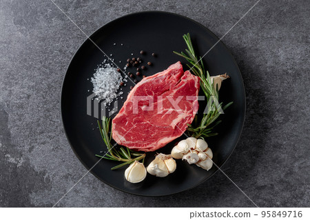 Raw beef steak with rosemary, garlic, salt, and pepper. 95849716