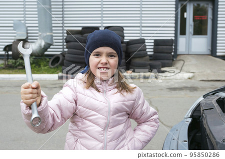 Portrait of a little girl with a wrench on the background of a car service. Children's auto mechanic. Automobile Repair Service Concept 95850286
