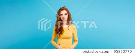 Portrait of young beautiful ginger woman with tender serious face crossing arms looking at camera. Isolated on pastel blue background. Copy space Portrait of young beautiful ginger woman with tender serious face crossing arms looking at camera. Isolated on pastel blue background. Copy space 95850770