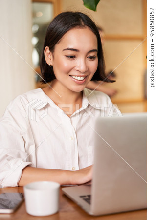 Stylish brunette woman with laptop, sitting in cafe and drinking coffee, smiling happily Stylish brunette woman with laptop, sitting in cafe and drinking coffee, smiling happily 95850852