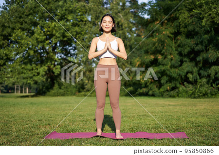 Young asian woman in sportswear, holding hands in namaste gesture, practice yoga, meditating and relaxing on fresh air in park, concept of mindfulness and wellbeing 95850866