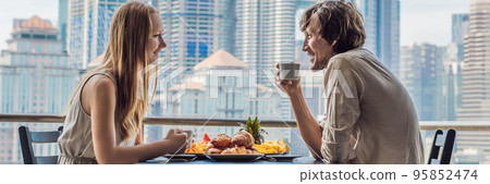 Loving couple having breakfast on the balcony. Breakfast table with coffee fruit and bread croisant on a balcony against the backdrop of the big city BANNER long format Loving couple having breakfast on the balcony. Breakfast table with coffee fruit and bread croisant on a balcony against the backdrop of the big city BANNER long format 95852474