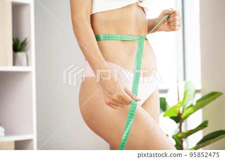 Slim young girl taking measurements of her body Slim young girl taking measurements of her body 95852475