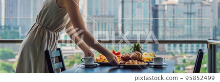 Young woman is laying on a table. Breakfast table with coffee fruit and bread croisant on a balcony against the backdrop of the big city BANNER, long format Young woman is laying on a table. Breakfast table with coffee fruit and bread croisant on a balcony against the backdrop of the big city BANNER, long format 95852499