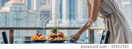 Young woman is laying on a table. Breakfast table with coffee fruit and bread croisant on a balcony against the backdrop of the big city BANNER, long format Young woman is laying on a table. Breakfast table with coffee fruit and bread croisant on a balcony against the backdrop of the big city BANNER, long format 95852501