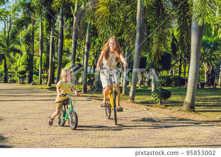 Happy family is riding bikes outdoors and smiling. Mom on a bike and son on a balancebike 95853002