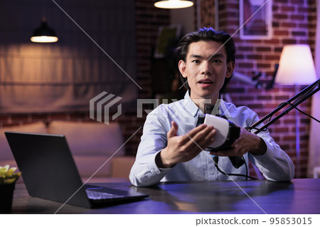 Male freelancer filming product review video with headphones, recommending audio headset to channel audience. Recording online recommendation vlog with podcast equipment station. Male freelancer filming product review video with headphones, recommending audio headset to channel audience. Recording online recommendation vlog with podcast equipment station. 95853015