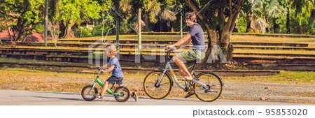 Happy family is riding bikes outdoors and smiling. Father on a bike and son on a balancebike BANNER, long format Happy family is riding bikes outdoors and smiling. Father on a bike and son on a balancebike BANNER, long format 95853020