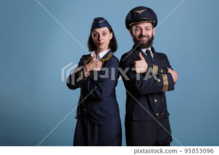 Smiling airplane pilot and flight attendant showing thumbs up gesture portrait, airplane crew in professional uniform looking at camera. Plane captain and air hostess with approval sign 95853096