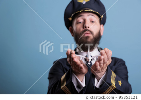 Airplane captain in uniform holding plane model in palms front view, pilot playing with commercial passenger jet toy. Professional aviation academy aviator on blue background Airplane captain in uniform holding plane model in palms front view, pilot playing with commercial passenger jet toy. Professional aviation academy aviator on blue background 95853121