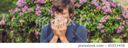 Young man sneezes because of an allergy to pollen BANNER long format Young man sneezes because of an allergy to pollen BANNER long format 95853456