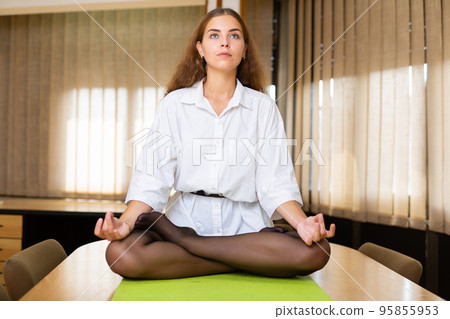 Relaxed young woman sitting in lotus position on office desk 95855953
