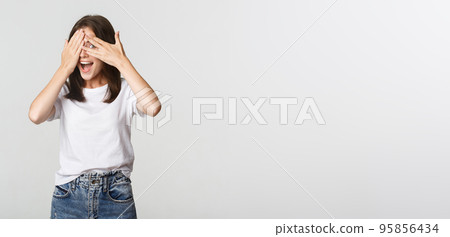 Excited and curious girl shut eyes and peeking through fingers amused Excited and curious girl shut eyes and peeking through fingers amused 95856434