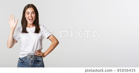 Friendly smiling girl waving hand to say hi, greeting someone 95856435