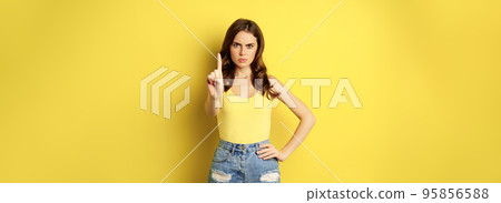Serious stylish woman showing stop, rejection, prohibition gesture, decline something, disapprove, standing over yellow background 95856588