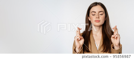 Hopeful saleswoman, corporate woman cross fingers and praying, yearning to achieve smth, standing in suit over white background Hopeful saleswoman, corporate woman cross fingers and praying, yearning to achieve smth, standing in suit over white background 95856987