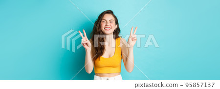 Summer holidays and emotions concept. Happy beautiful girl showing peace v-signs and having fun, laughing and smiling at camera, standing against blue background Summer holidays and emotions concept. Happy beautiful girl showing peace v-signs and having fun, laughing and smiling at camera, standing against blue background 95857137