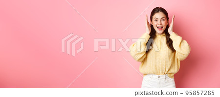 Cheerful young woman smiling, looking excited, open her ears after loud bang or fireworks, celebrating something, standing against pink bright background Cheerful young woman smiling, looking excited, open her ears after loud bang or fireworks, celebrating something, standing against pink bright background 95857285