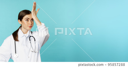 Portrait of annoyed, tired woman doctor, facepalm, roll eyes frustrated, bothered by smth stupid, standing in white coat over torquoise background Portrait of annoyed, tired woman doctor, facepalm, roll eyes frustrated, bothered by smth stupid, standing in white coat over torquoise background 95857288