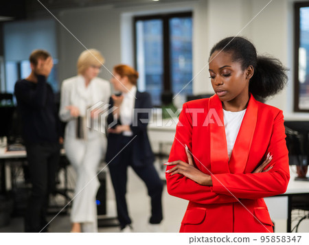 Young african woman is upset because of the ridicule of colleagues. Racial discrimination in the office. Young african woman is upset because of the ridicule of colleagues. Racial discrimination in the office. 95858347
