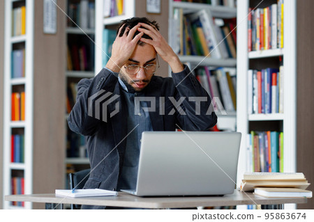 Man having stress while using laptop in library 95863674