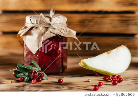 Jar of homemade lingonberry and pear jam with craft paper on lid on wooden table next to fresh lingonberries and pears Jar of homemade lingonberry and pear jam with craft paper on lid on wooden table next to fresh lingonberries and pears 95865606