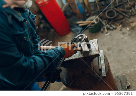 Blacksmith forges and makes metal detail with hammer and anvil at forge Blacksmith forges and makes metal detail with hammer and anvil at forge 95867391