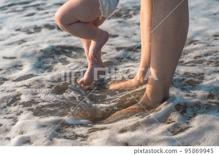 Baby walks on the sea beach and learns to walk with his mother. First steps, parental care and love concept 95869945