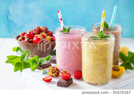 Strawberry, chocolate and apricot milkshake or smoothies on a white wooden background. Healthy juicy vitamin drink diet or vegan food concept. Copy space. 95870267