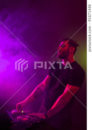 Attractive young DJ playing on turntables with color light effects 95871486