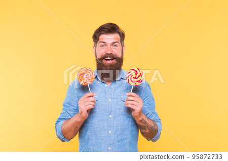 Happy bearded man hold tasty rainbow swirl candy pops great for birthday party and candy buffet yellow background, celebration Happy bearded man hold tasty rainbow swirl candy pops great for birthday party and candy buffet yellow background, celebration 95872733