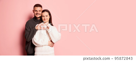 Portrait of lovely young couple, man and woman, making heart shape with hands, posing isolated over pink background Portrait of lovely young couple, man and woman, making heart shape with hands, posing isolated over pink background 95872843