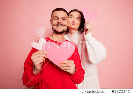Portrait of lovely young couple, man and woman posing with paper hearts isolated over pink background. Happiness Portrait of lovely young couple, man and woman posing with paper hearts isolated over pink background. Happiness 95872845