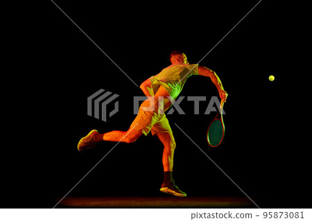Young sportive man, professional tennis player in motion, action isolated over dark background in neon light. Concept of professional sport, competition, skills. Young sportive man, professional tennis player in motion, action isolated over dark background in neon light. Concept of professional sport, competition, skills. 95873081