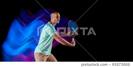 Movements in neon glow. Active male tennis player in sportwear playing tennis isolated over dark background in mixed purple neon light. Movements in neon glow. Active male tennis player in sportwear playing tennis isolated over dark background in mixed purple neon light. 95873088
