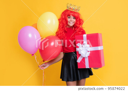 happy girl in crown with present box and party balloon on yellow background happy girl in crown with present box and party balloon on yellow background 95874022