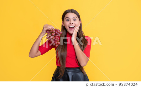 glad amazed child hold bunch of grapes on yellow background 95874024