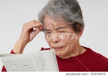 A senior woman who seems to have difficulty reading newspapers due to presbyopia 95874970