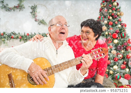 Father playing guitar during christmas. Happy man 60s playing guitar christmas songs. Father playing guitar during christmas. Happy man 60s playing guitar christmas songs. 95875231