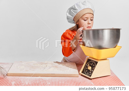 Cute little child, girl in image of chef cooking over grey background. Measuring flour Cute little child, girl in image of chef cooking over grey background. Measuring flour 95877173
