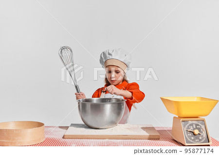 Cute little child, girl in image of chef cooking over grey background. Making dough Cute little child, girl in image of chef cooking over grey background. Making dough 95877174