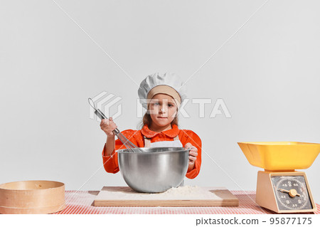 Cute little child, girl in image of chef cooking over grey background. Mixing dough Cute little child, girl in image of chef cooking over grey background. Mixing dough 95877175