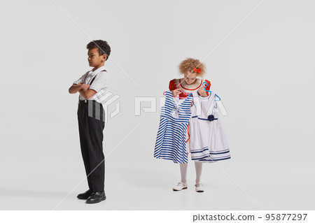 Portrait of stylish children, boy in suit and girl choosing dress to wear isolated over grey background Portrait of stylish children, boy in suit and girl choosing dress to wear isolated over grey background 95877297