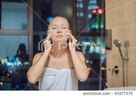 Beautiful woman removes makeup on the background of a window with a panoramic view of the night city 95877570