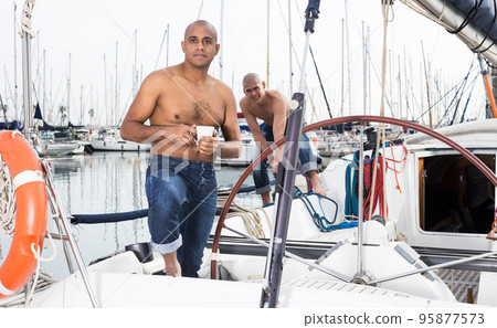 Latin American topless with a cup of coffee in his hand standing on the deck of a yacht in the seaport 95877573