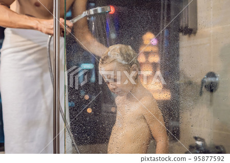 Dad washes his son's hair in the shower in the evening before going to sleep on the background of a window with a panoramic view of the city Dad washes his son's hair in the shower in the evening before going to sleep on the background of a window with a panoramic view of the city 95877592