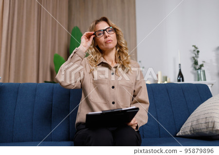 Portrait of confident mature female psychologist sitting on sofa at home 95879896