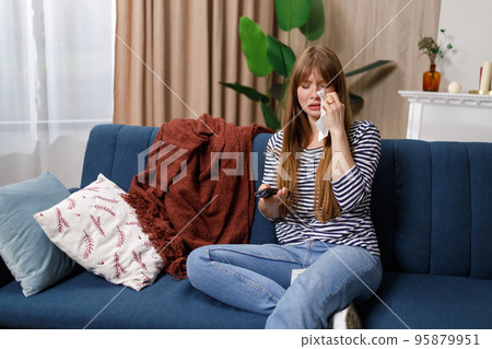 Crying woman wiping tears while watching tv at home Crying woman wiping tears while watching tv at home 95879951